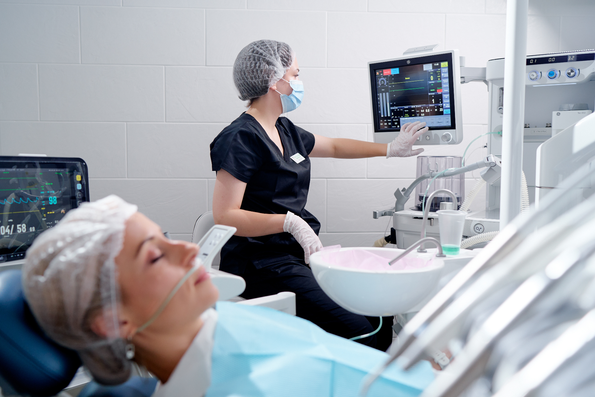Anesthesia provider monitoring vital signs during dental IV sedation with patient resting calmly in the chair